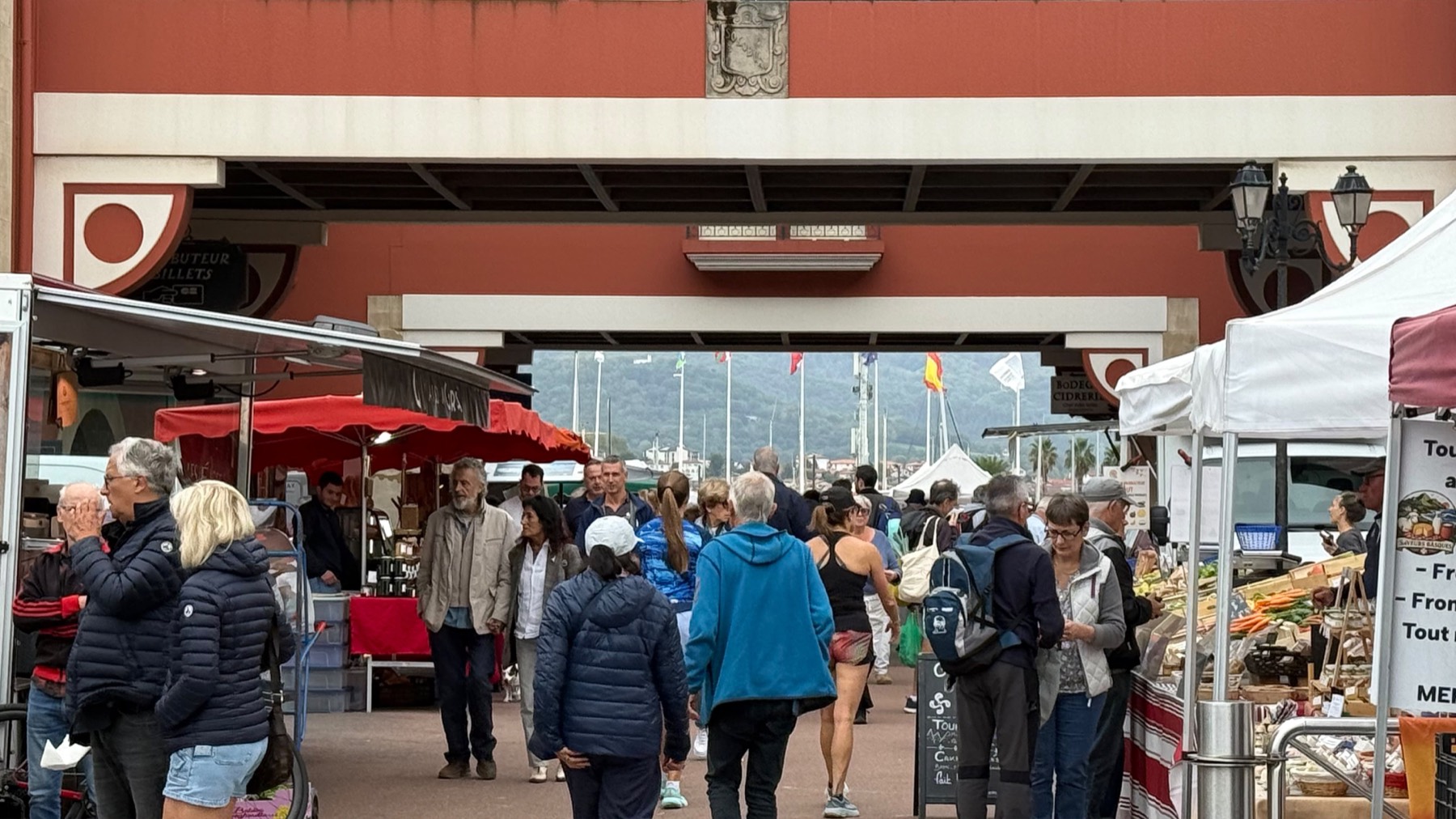 Gente paseando entre los puestos del mercado de Hendaya, con el puerto al fondo